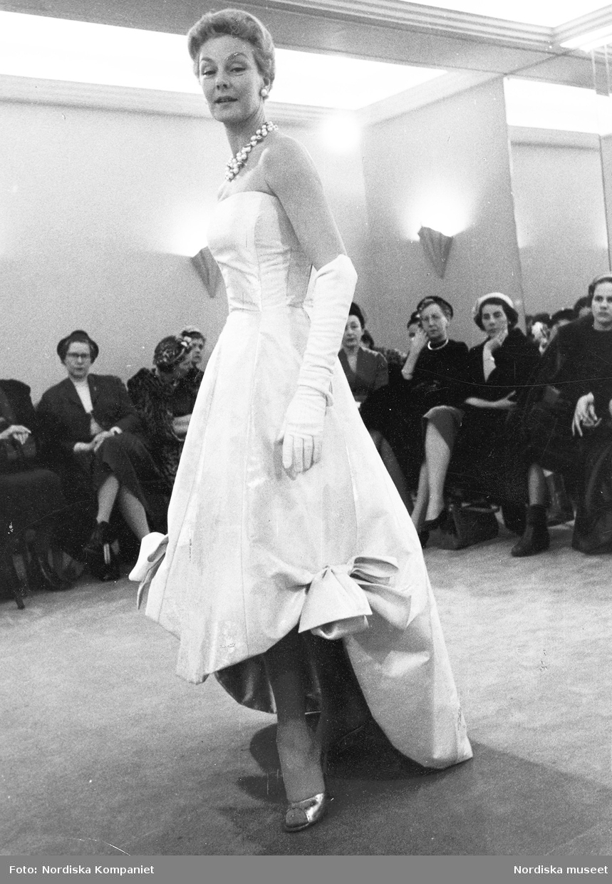 Modevisning. Margareta Nordlund i ljus aftonklänning med rosetter, vita ...