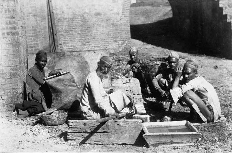 Blacksmiths at work at the Kumaon Iron Works in India. From left to right you can see the bellows, a basket of charcoal and a hammer. On the right in the foreground water for hardening.
